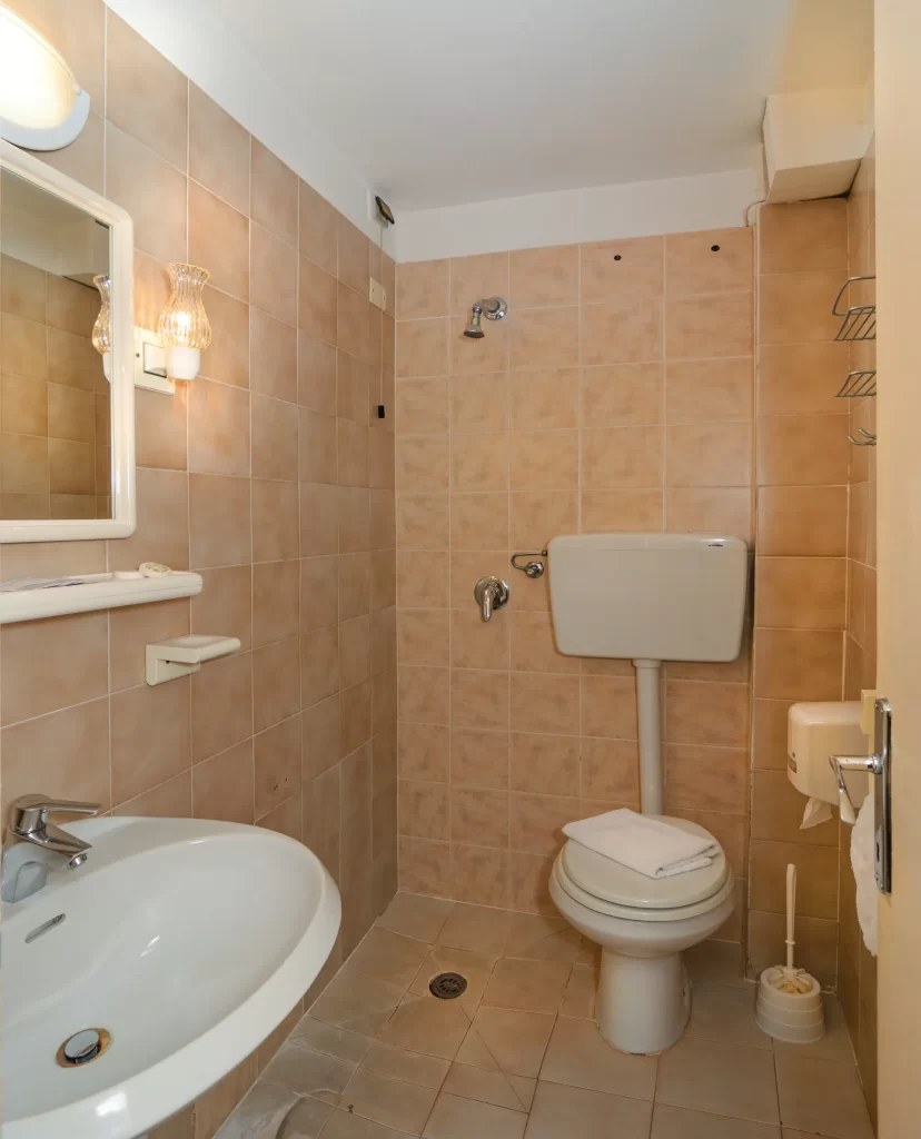 Bagno con WC, doccia e lavandino, arredamento essenziale con piastrelle beige.