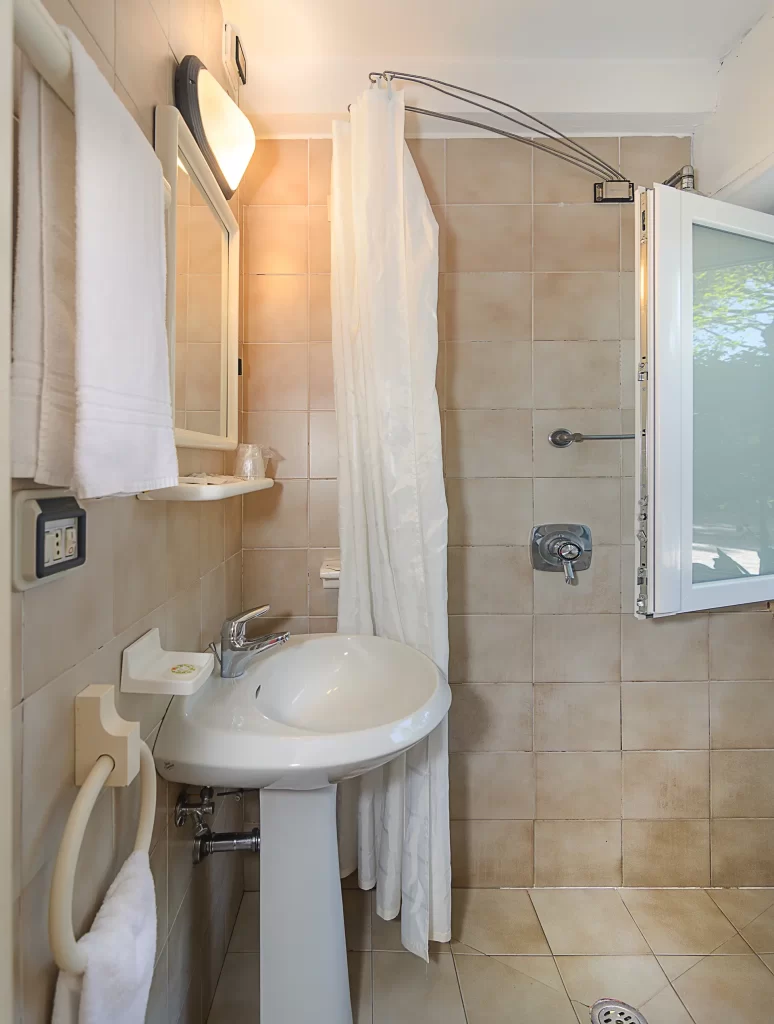 Bagno privato con lavandino e doccia con piastrelle beige e finestra aperta.