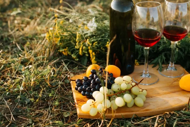 Degustazione di vino rosso con grappoli d'uva e frutta in un'atmosfera rustica all'aperto.