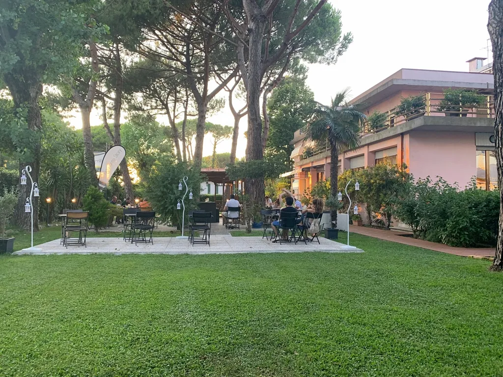 Giardino dell'hotel con tavolini all'aperto, alberi e atmosfera rilassante al tramonto.