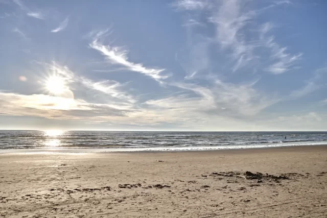 Spiaggia di Forte dei Marmi con il sole al tramonto e mare calmo sotto un cielo azzurro.