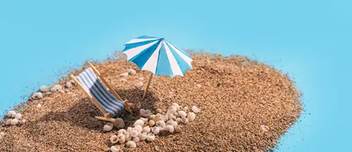 Miniatura di spiaggia con sdraio, ombrellone e conchiglie su sabbia, sfondo azzurro estivo.