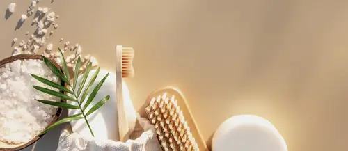 Set di prodotti spa naturali con spazzole, sale e sapone su sfondo beige illuminato dal sole.